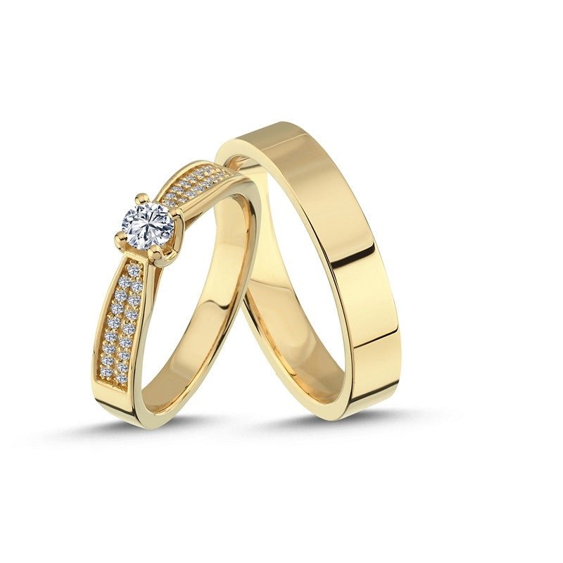 Luksuriøse Nuran vielsesringe i 14 kt guld med 0,60 ct diamanter – damering med central diamant og mindre sten, herrering i blankpoleret bredt guld.